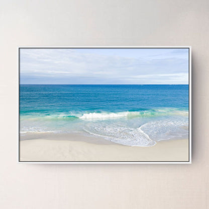 White framed canvas print of aerial photography of Alkimos Beach, a small wave rolling onto pale sand beneath a blue sea and cloudy sky
