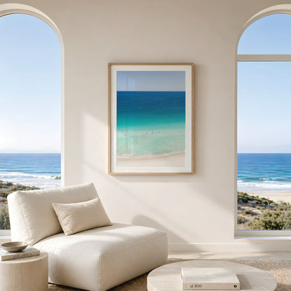 Framed canvas print of aerial photography of Scarborough Beach, deep blue ocean meeting turquoise shallows and a white sand beach with small figures in portrait orientation hanging in a living room