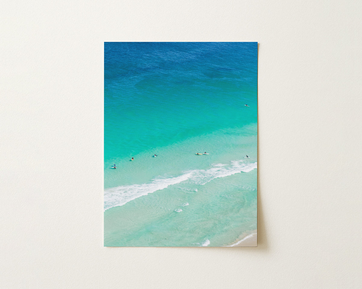 Fine art paper print of aerial photography of Scarborough Beach, surfers and swimmers in deep turquoise water along a diagonal shoreline in portrait orientation