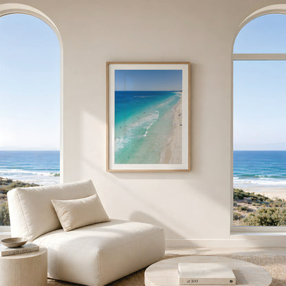 Framed canvas print of aerial photography of Scarborough Beach, deep blue water, turquoise shallows and pale sand along a diagonal shore in portrait orientation hanging in a living room