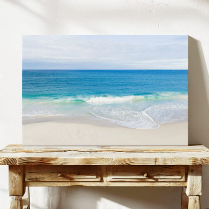Stretched canvas print of aerial photography of Alkimos Beach, a small wave rolling onto pale sand beneath a blue sea and cloudy sky on a console table