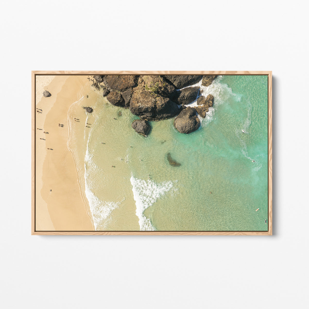 Oak framed canvas print of aerial photography of Dreamtime Beach, a dark rock outcrop beside golden sand and green water