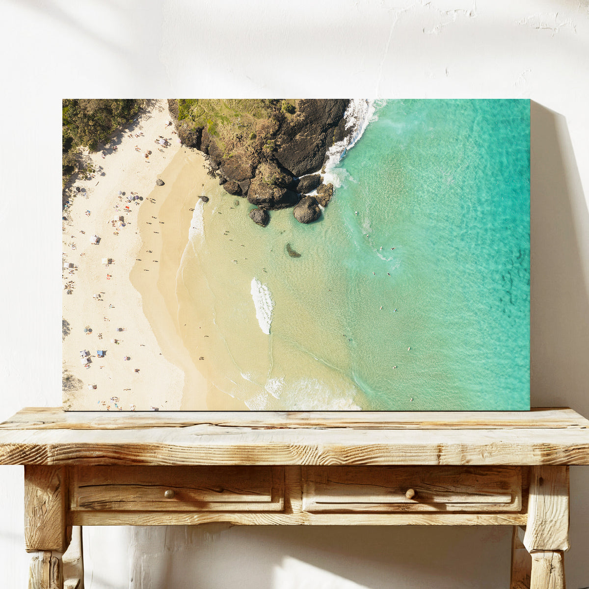 Stretched canvas print of aerial photography of Dreamtime Beach, headland rocks with sand, turquoise water and a small white boat on a console table