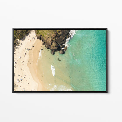 Black framed canvas print of aerial photography of Dreamtime Beach, headland rocks with sand, turquoise water and a small white boat