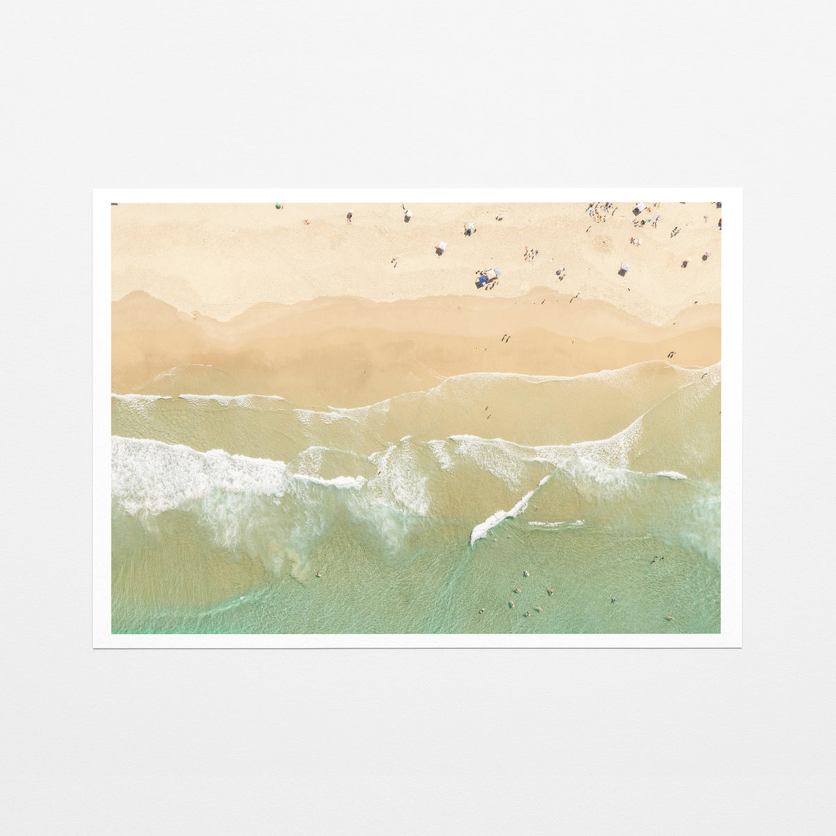 Fine art paper print of aerial photography of Dreamtime Beach, soft shoreline wash over pale sand with people on the beach with a white border