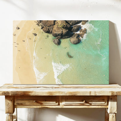 Stretched canvas print of aerial photography of Dreamtime Beach, a dark rock outcrop beside golden sand and green water on a console table