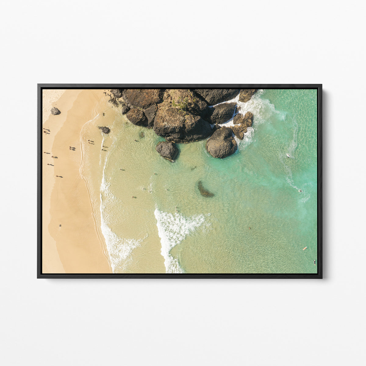 Black framed canvas print of aerial photography of Dreamtime Beach, a dark rock outcrop beside golden sand and green water