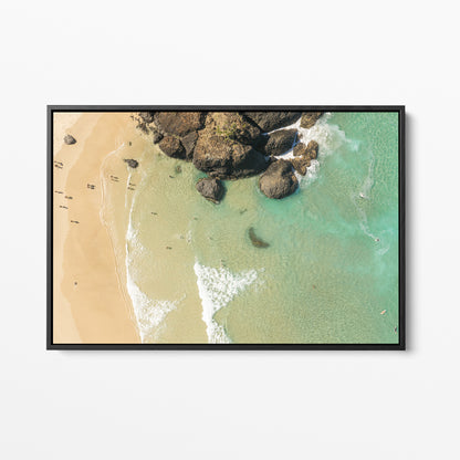 Black framed canvas print of aerial photography of Dreamtime Beach, a dark rock outcrop beside golden sand and green water