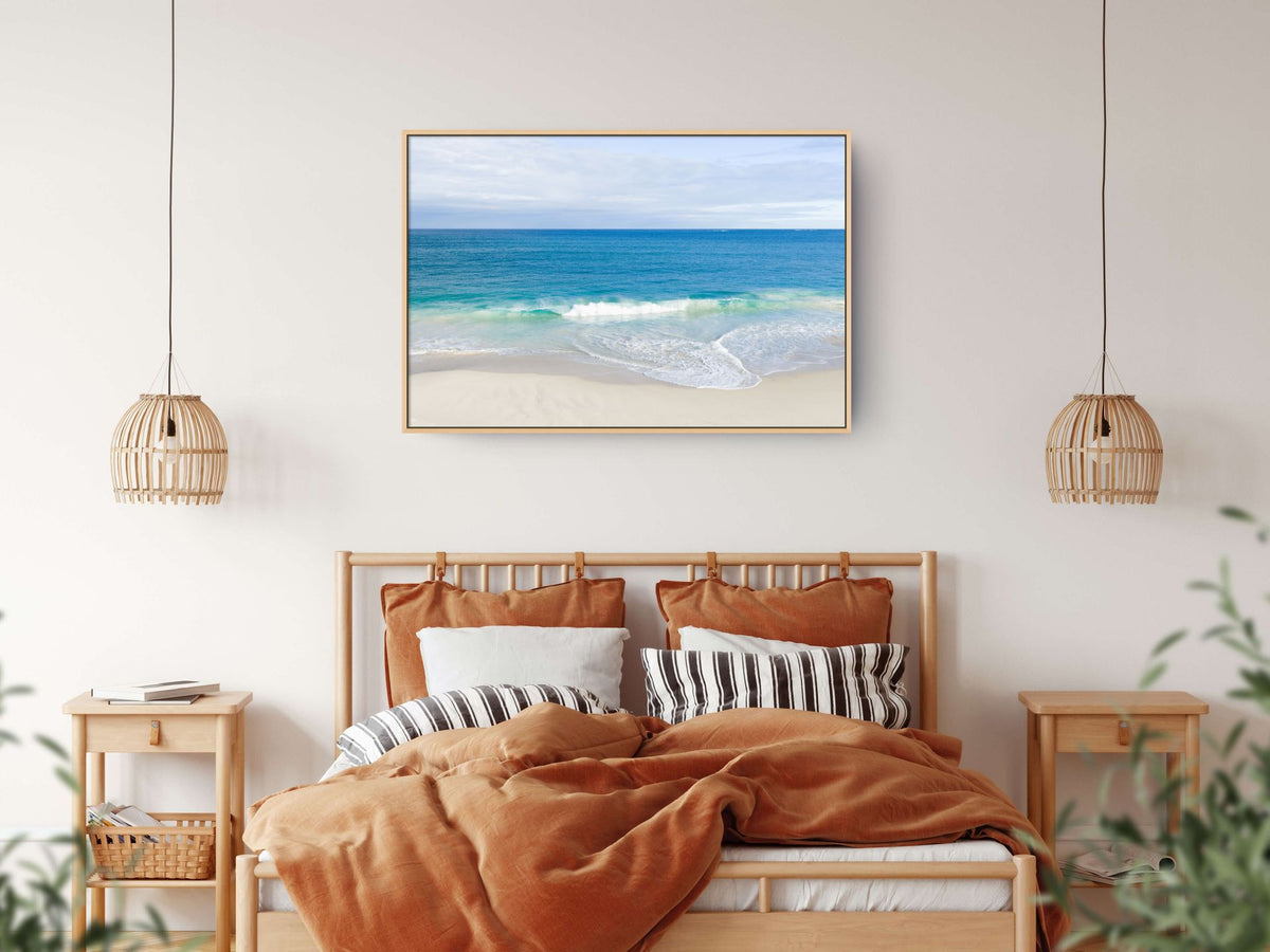 Canvas print of aerial photography of Alkimos Beach, a small wave rolling onto pale sand beneath a blue sea and cloudy sky hanging above a bed in a bedroom