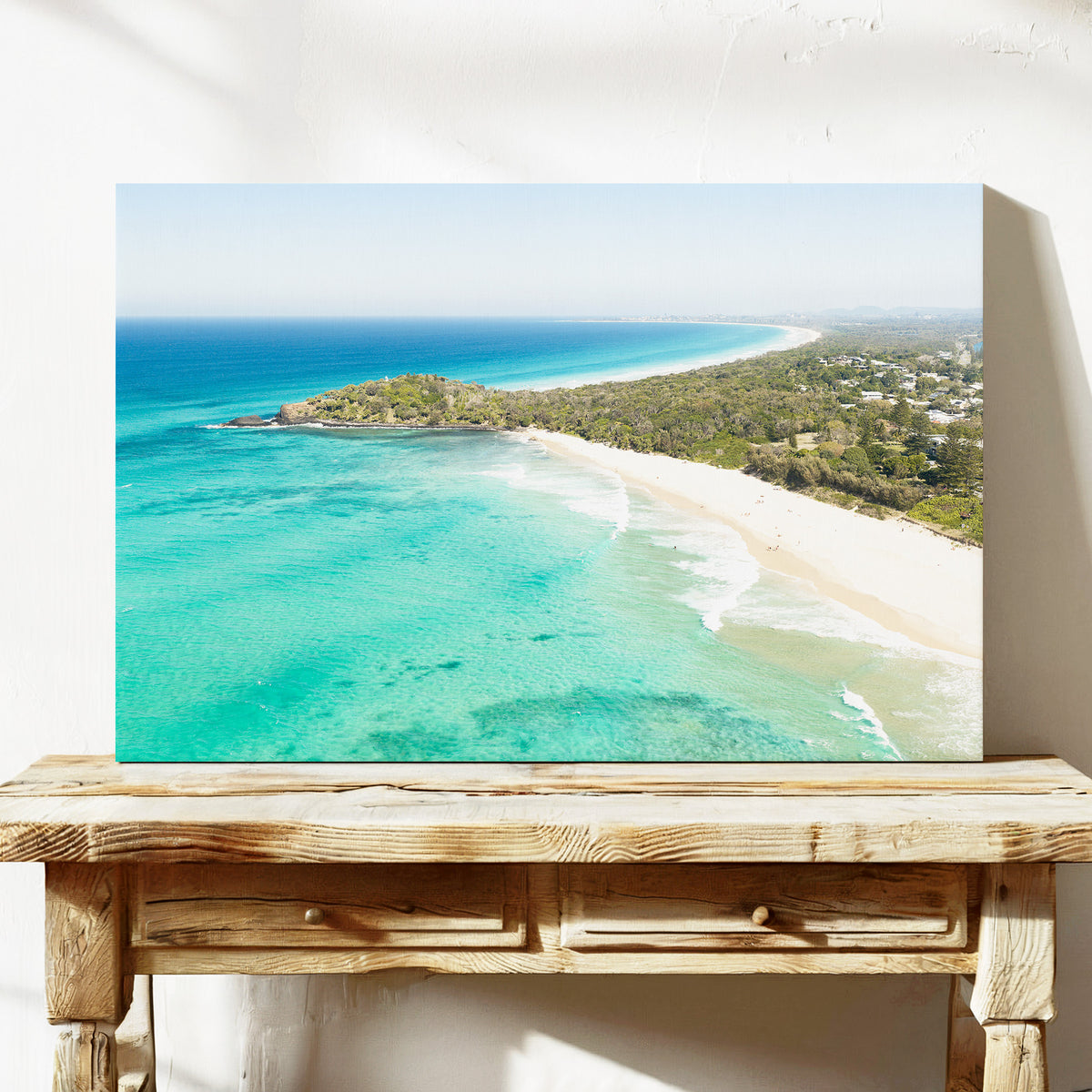 Stretched canvas print of aerial photography of Fingal Head, a bush covered headland with houses, a sandy beach and turquoise reef water on a console table