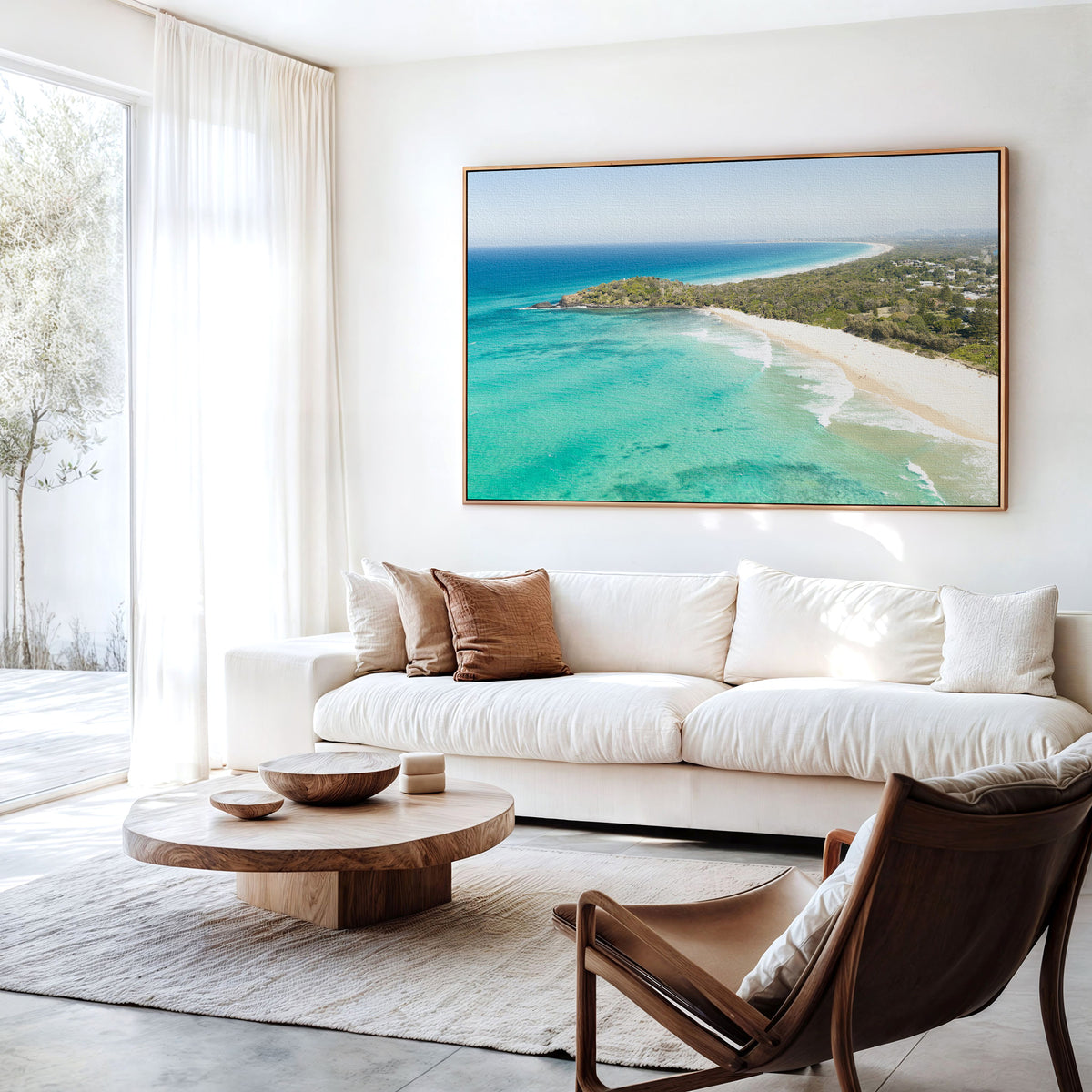 Canvas print of aerial photography of Fingal Head, a bush covered headland with houses, a sandy beach and turquoise reef water hanging above a sofa in a living room