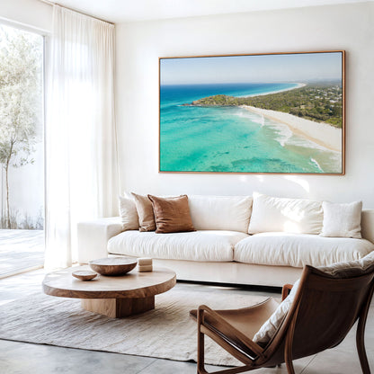 Canvas print of aerial photography of Fingal Head, a bush covered headland with houses, a sandy beach and turquoise reef water hanging above a sofa in a living room