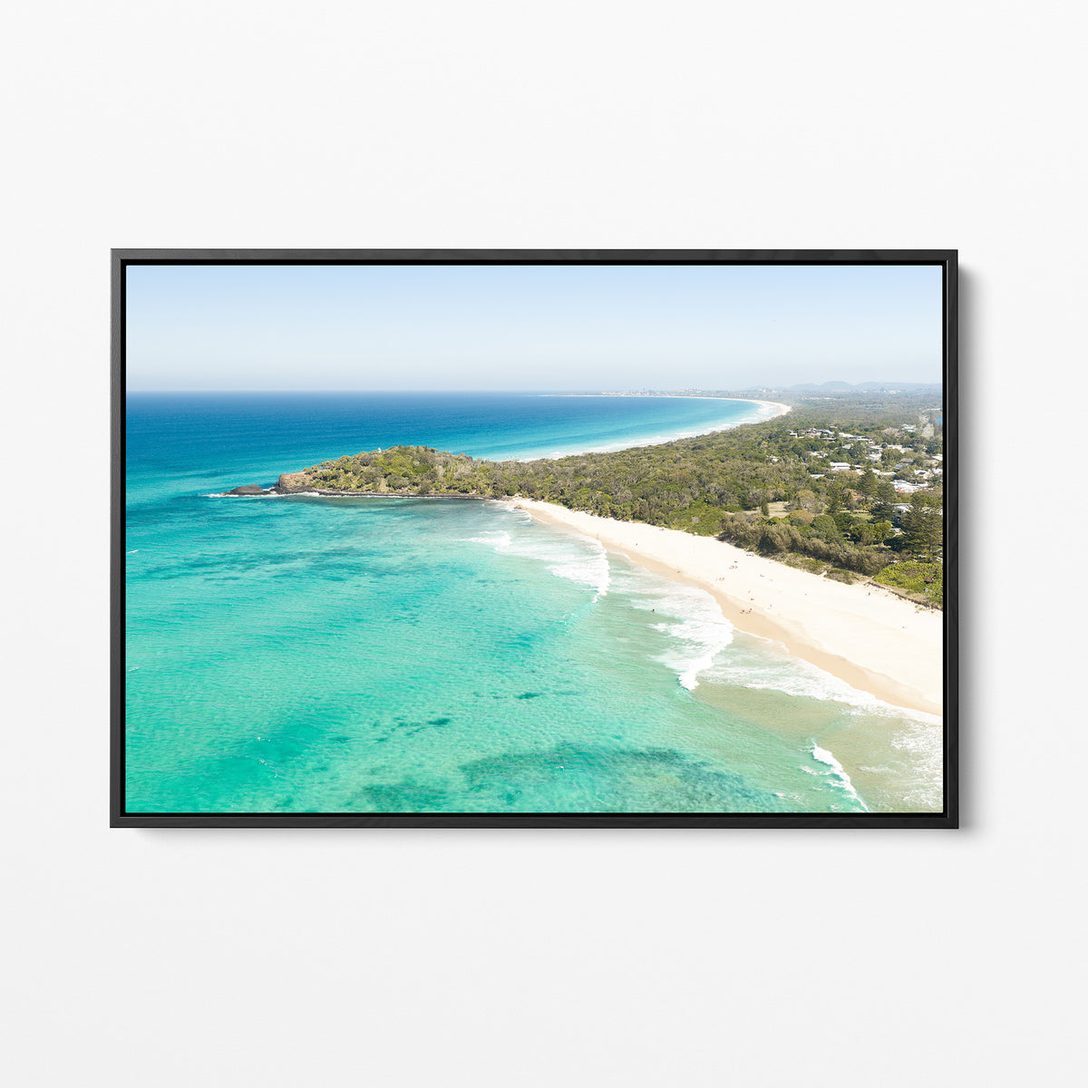 Black framed canvas print of aerial photography of Fingal Head, a bush covered headland with houses, a sandy beach and turquoise reef water