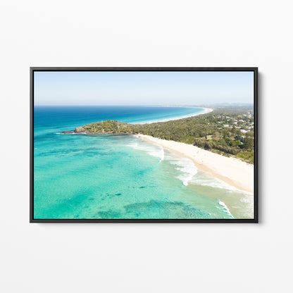 Black framed canvas print of aerial photography of Fingal Head, a bush covered headland with houses, a sandy beach and turquoise reef water