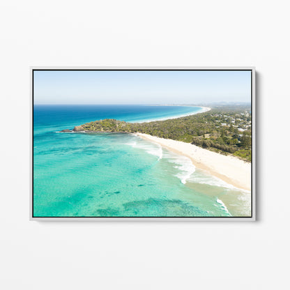 White framed canvas print of aerial photography of Fingal Head, a bush covered headland with houses, a sandy beach and turquoise reef water