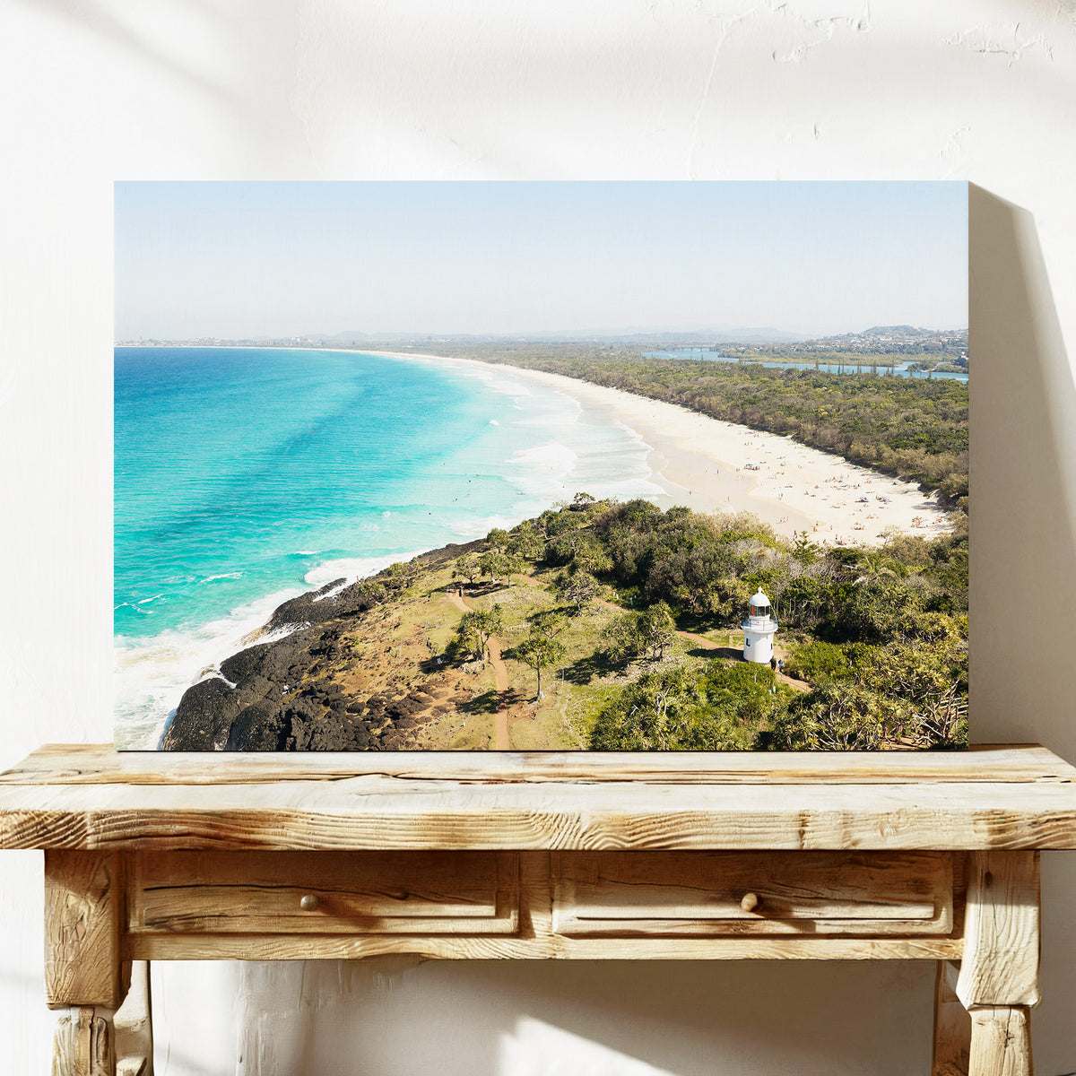 Stretched canvas print of aerial photography of Fingal Head Lighthouse, a white lighthouse on a bush headland above a long beach and turquoise sea on a console table