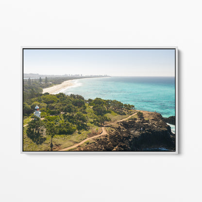 White framed canvas print of aerial photography of Fingal Head Lighthouse, bushland with a dirt track, a rocky cliff, the beach and turquoise sea