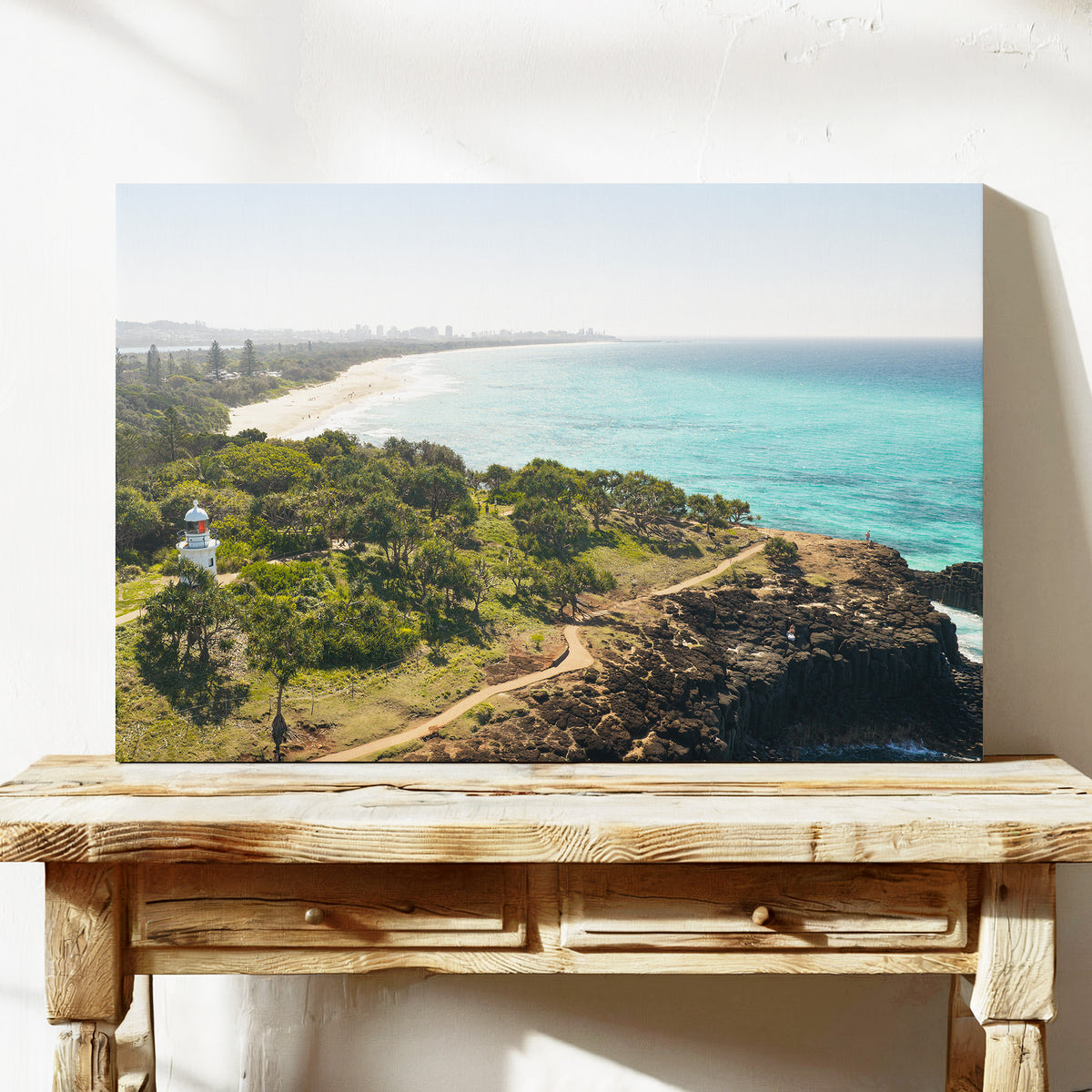 Stretched canvas print of aerial photography of Fingal Head Lighthouse, bushland with a dirt track, a rocky cliff, the beach and turquoise sea on a console table