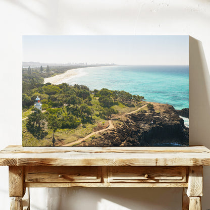 Stretched canvas print of aerial photography of Fingal Head Lighthouse, bushland with a dirt track, a rocky cliff, the beach and turquoise sea on a console table