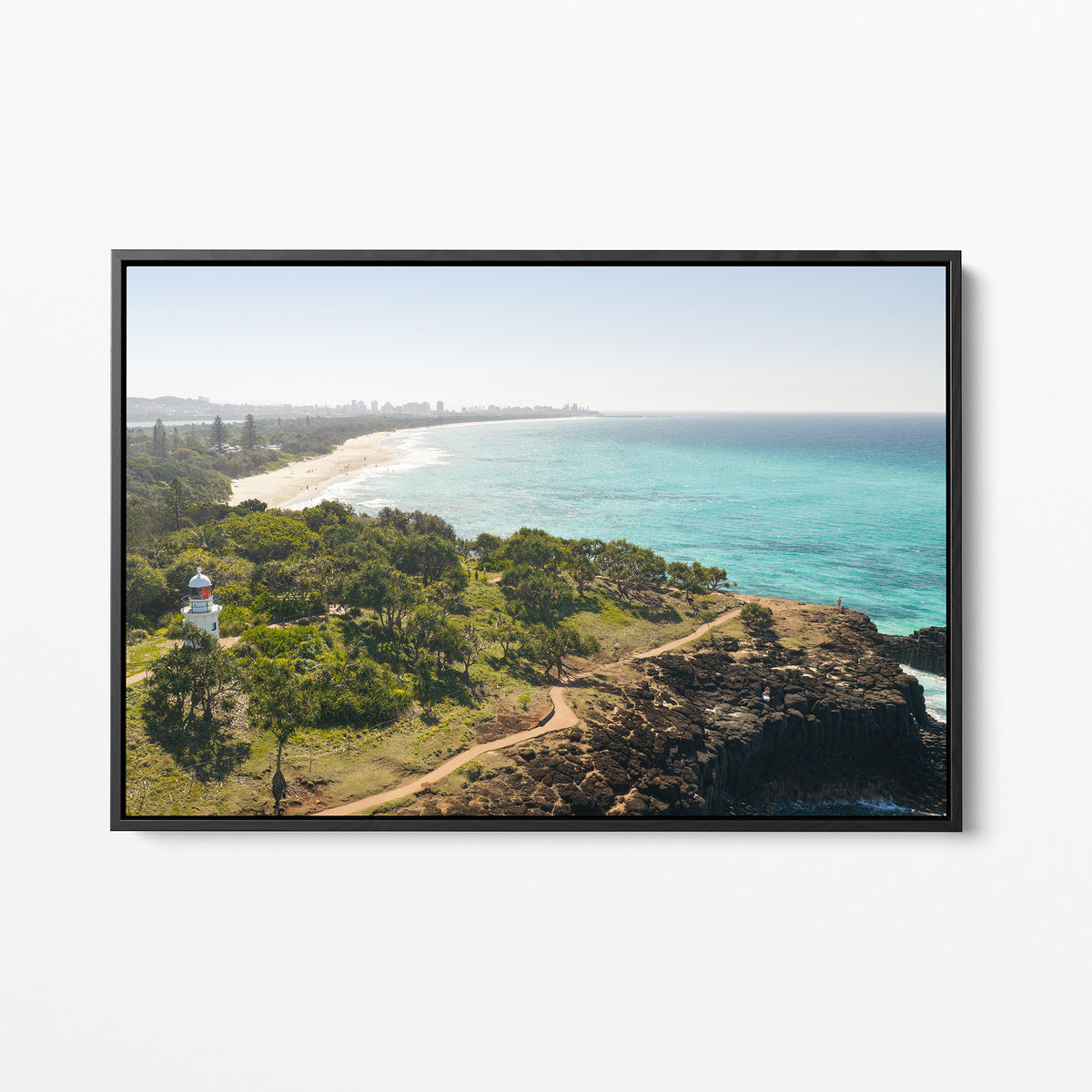 Black framed canvas print of aerial photography of Fingal Head Lighthouse, bushland with a dirt track, a rocky cliff, the beach and turquoise sea