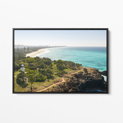 Black framed canvas print of aerial photography of Fingal Head Lighthouse, bushland with a dirt track, a rocky cliff, the beach and turquoise sea