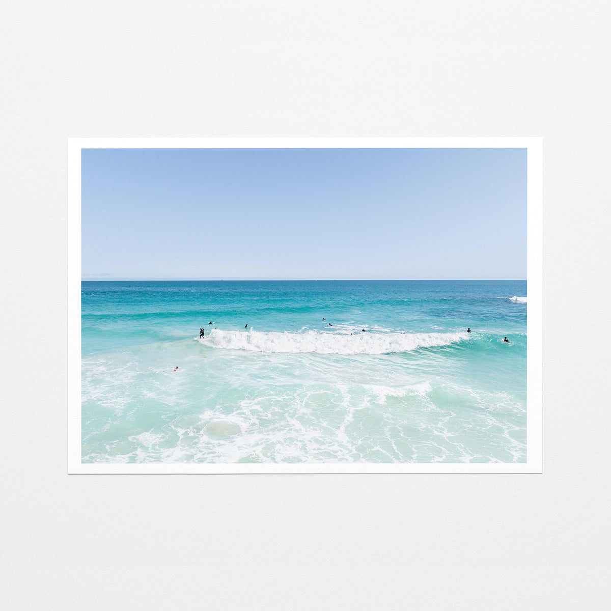 Fine art paper print of aerial photography of Scarborough Beach, a wide view of surfers spread across turquoise water and white foam with a white border