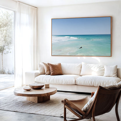 Canvas print of aerial photography of Scarborough Beach, a surfer lying on a board in clear turquoise shallows hanging above a sofa in a living room