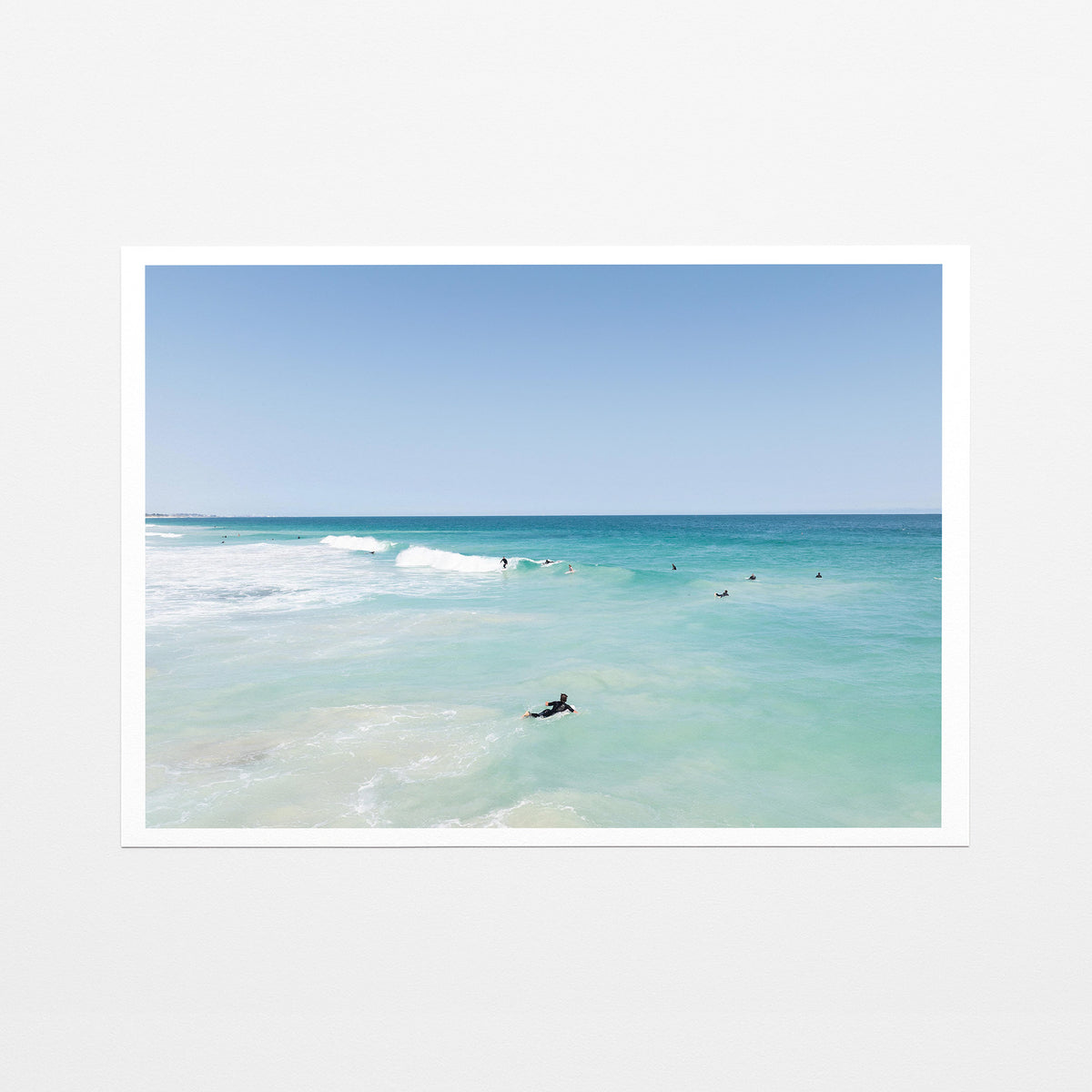 Fine art paper print of aerial photography of Scarborough Beach, a surfer lying on a board in clear turquoise shallows with a white border