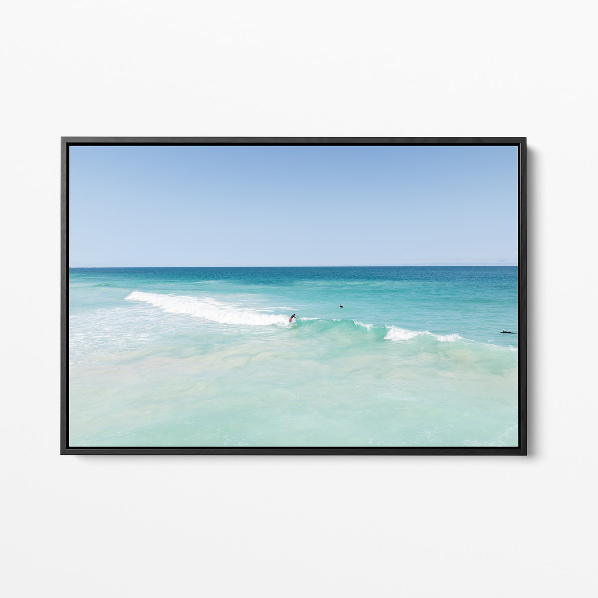 Black framed canvas print of aerial photography of Scarborough Beach, a surfer on a breaking wave in pale turquoise water