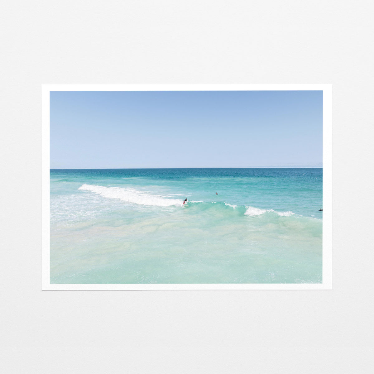 Fine art paper print of aerial photography of Scarborough Beach, a surfer on a breaking wave in pale turquoise water with a white border