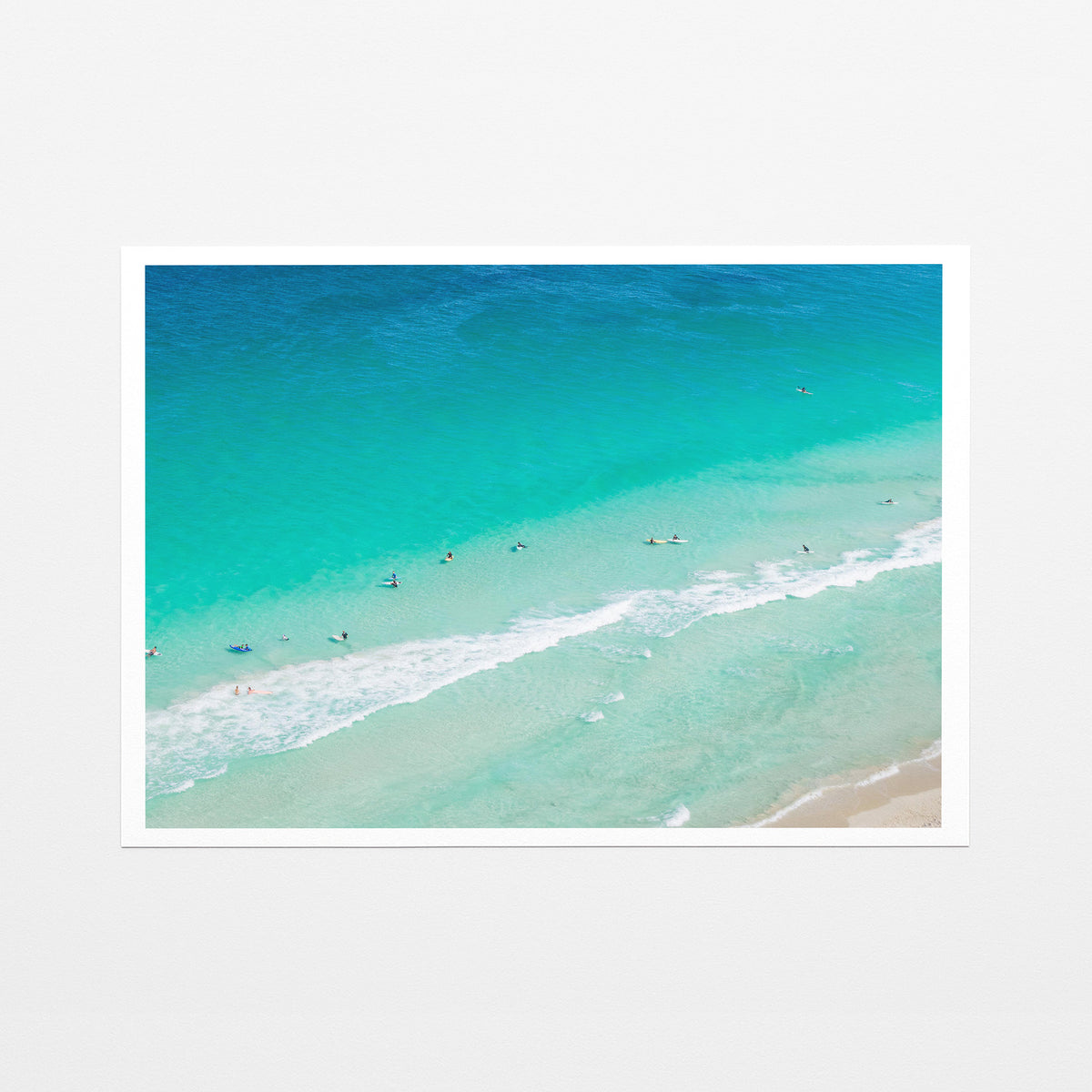 Fine art paper print of aerial photography of Scarborough Beach, surfers and swimmers in deep turquoise water along a diagonal shoreline with a white border