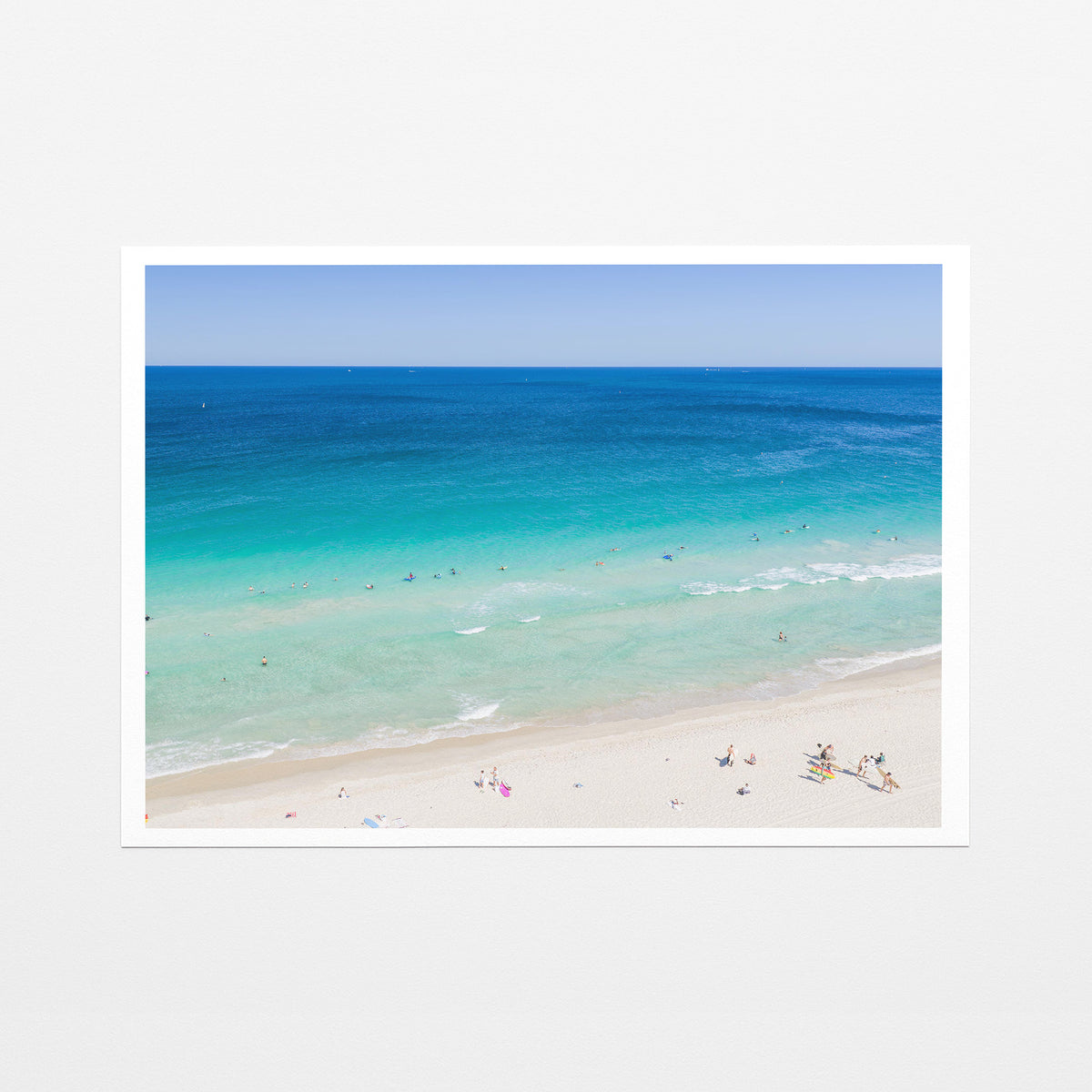 Fine art paper print of aerial photography of Scarborough Beach, deep blue ocean meeting turquoise shallows and a white sand beach with small figures with a white border