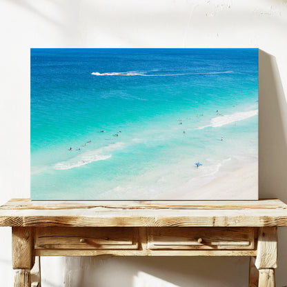 Stretched canvas print of aerial photography of Scarborough Beach, surfers in blue and turquoise water along a diagonal shoreline with white foam lines on a console table