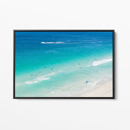 Black framed canvas print of aerial photography of Scarborough Beach, surfers in blue and turquoise water along a diagonal shoreline with white foam lines