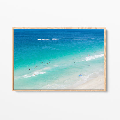Oak framed canvas print of aerial photography of Scarborough Beach, surfers in blue and turquoise water along a diagonal shoreline with white foam lines