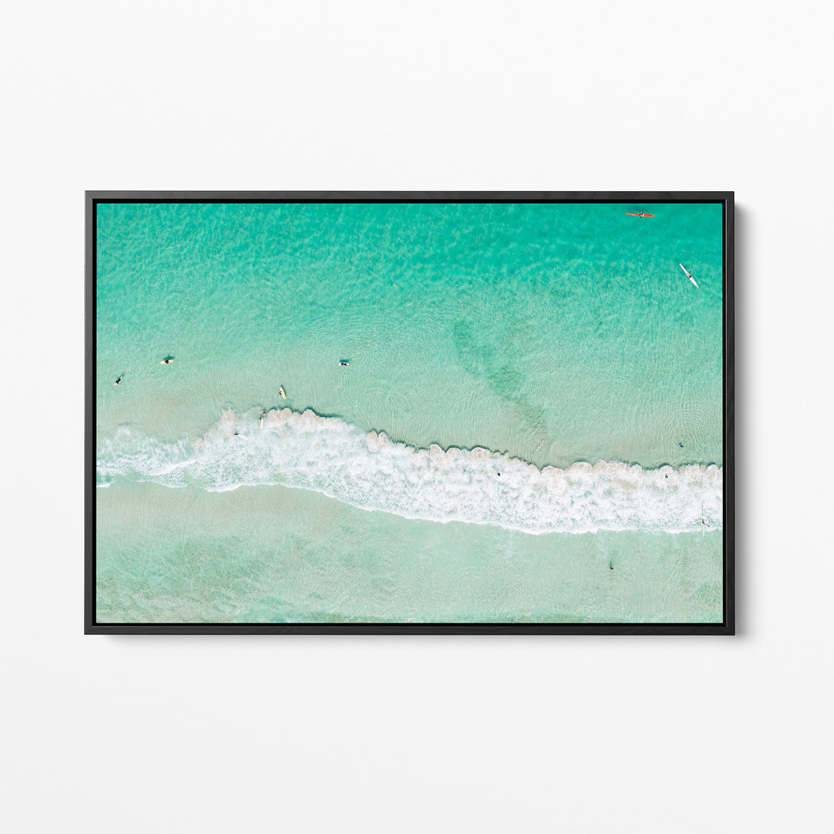Black framed canvas print of aerial photography of Scarborough Beach, a line of white wave across green turquoise shallows with shadows on the sea floor