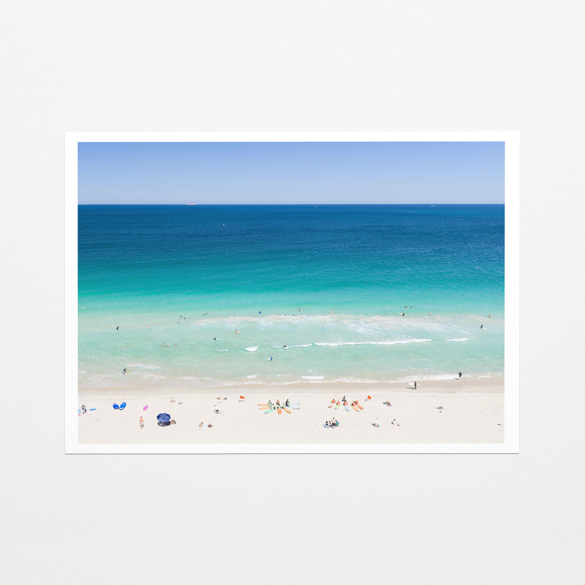 Fine art paper print of aerial photography of Scarborough Beach, colourful umbrellas and people on white sand beside turquoise water and deep blue ocean with a white border